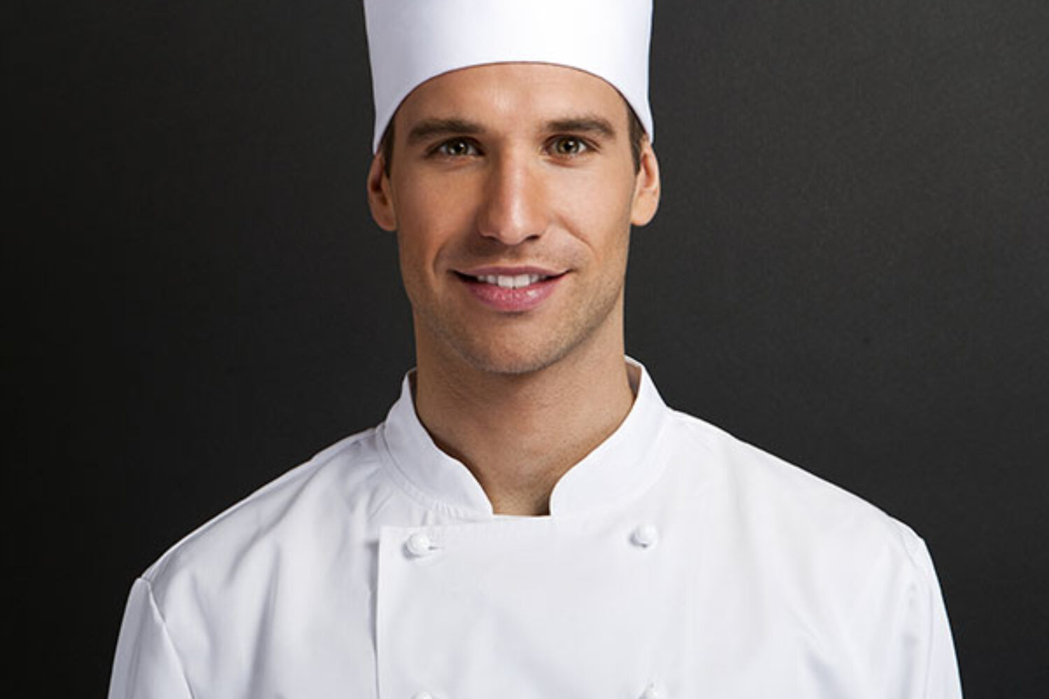 Portrait of a confident male chef in white uniform and tall hat.