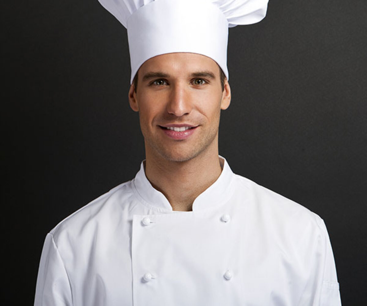 Portrait of a confident male chef in white uniform and tall hat.
