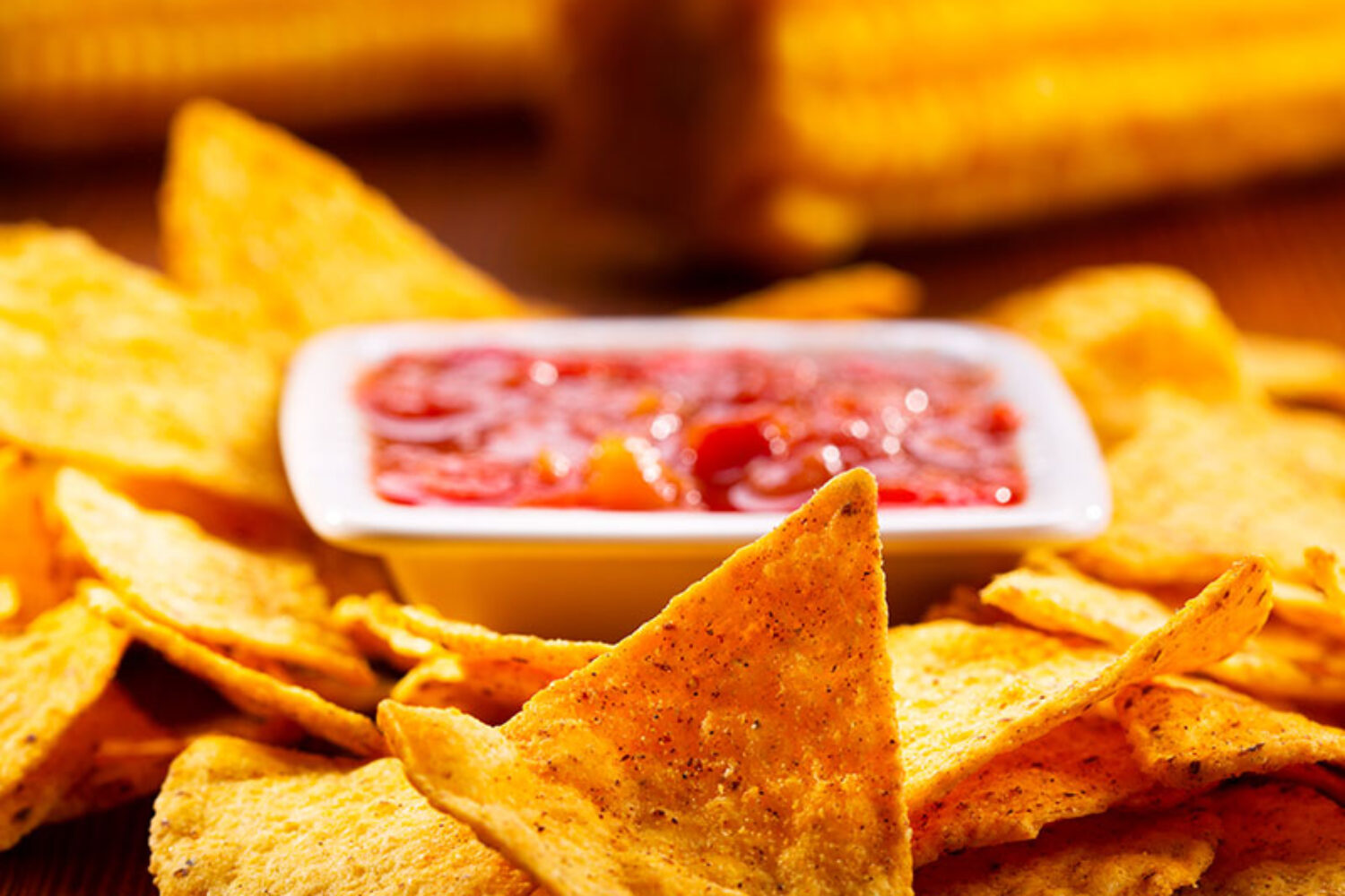 Close-up of tortilla chips with salsa and corn on the cob.