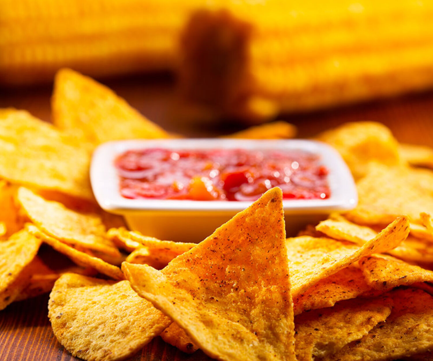 Close-up of tortilla chips with salsa and corn on the cob.
