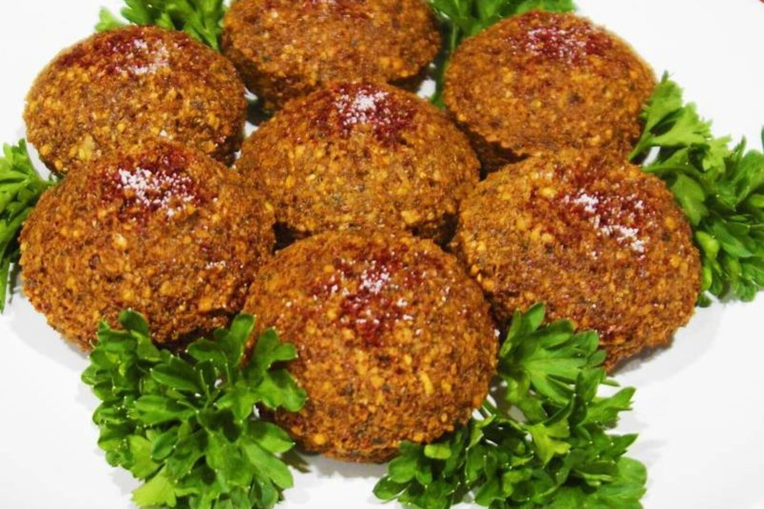 Spicy fried falafel balls garnished with parsley on a white plate.