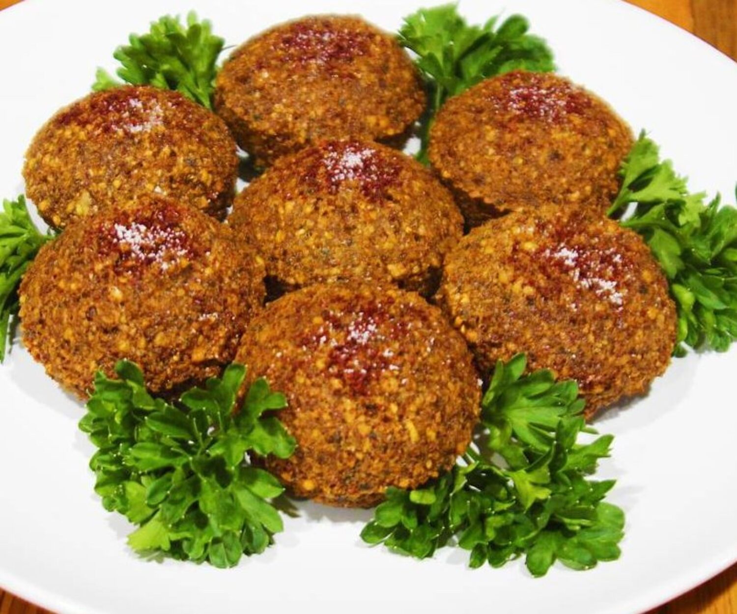 Spicy fried falafel balls garnished with parsley on a white plate.