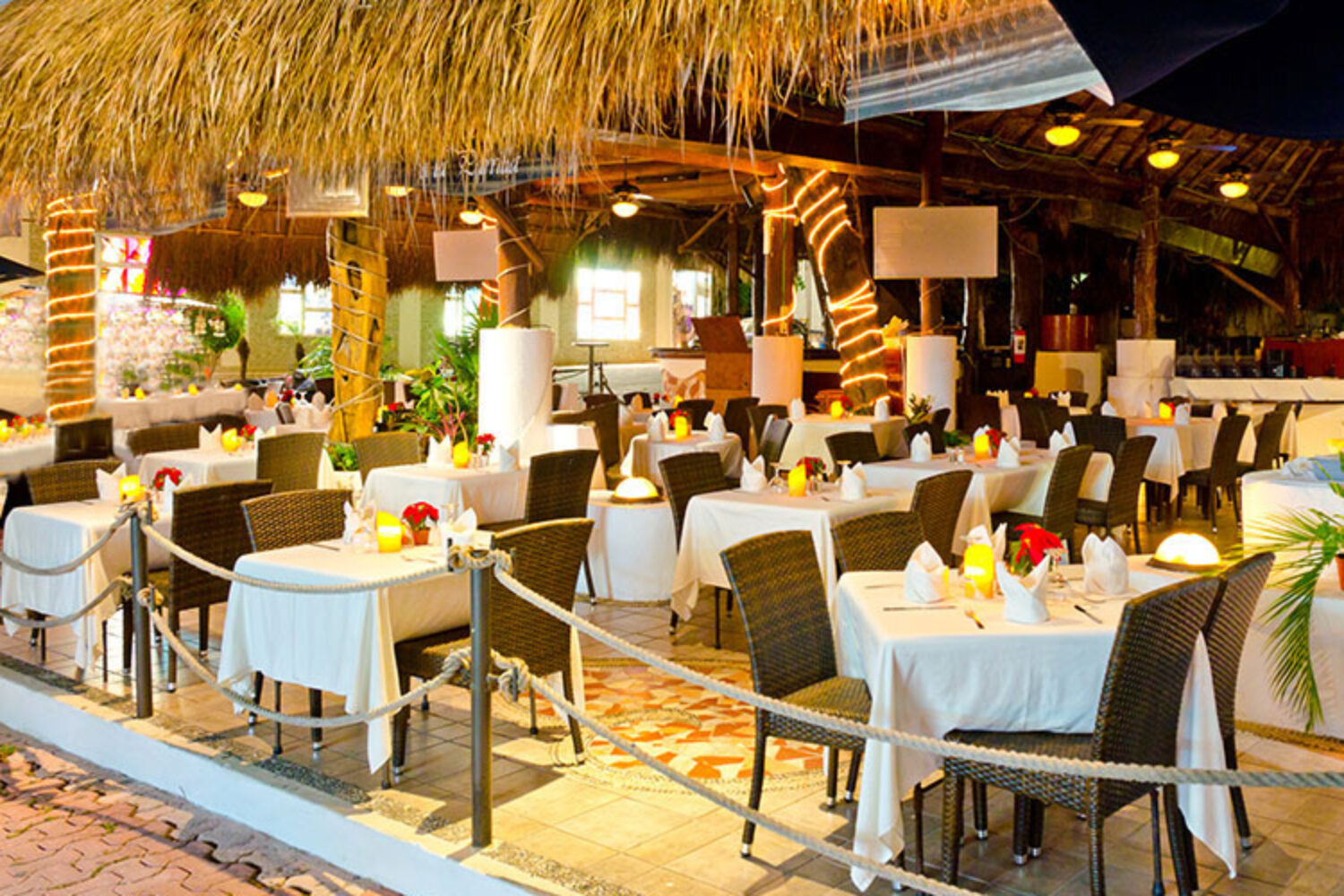 Elegant outdoor restaurant with neatly set tables under a thatched roof.