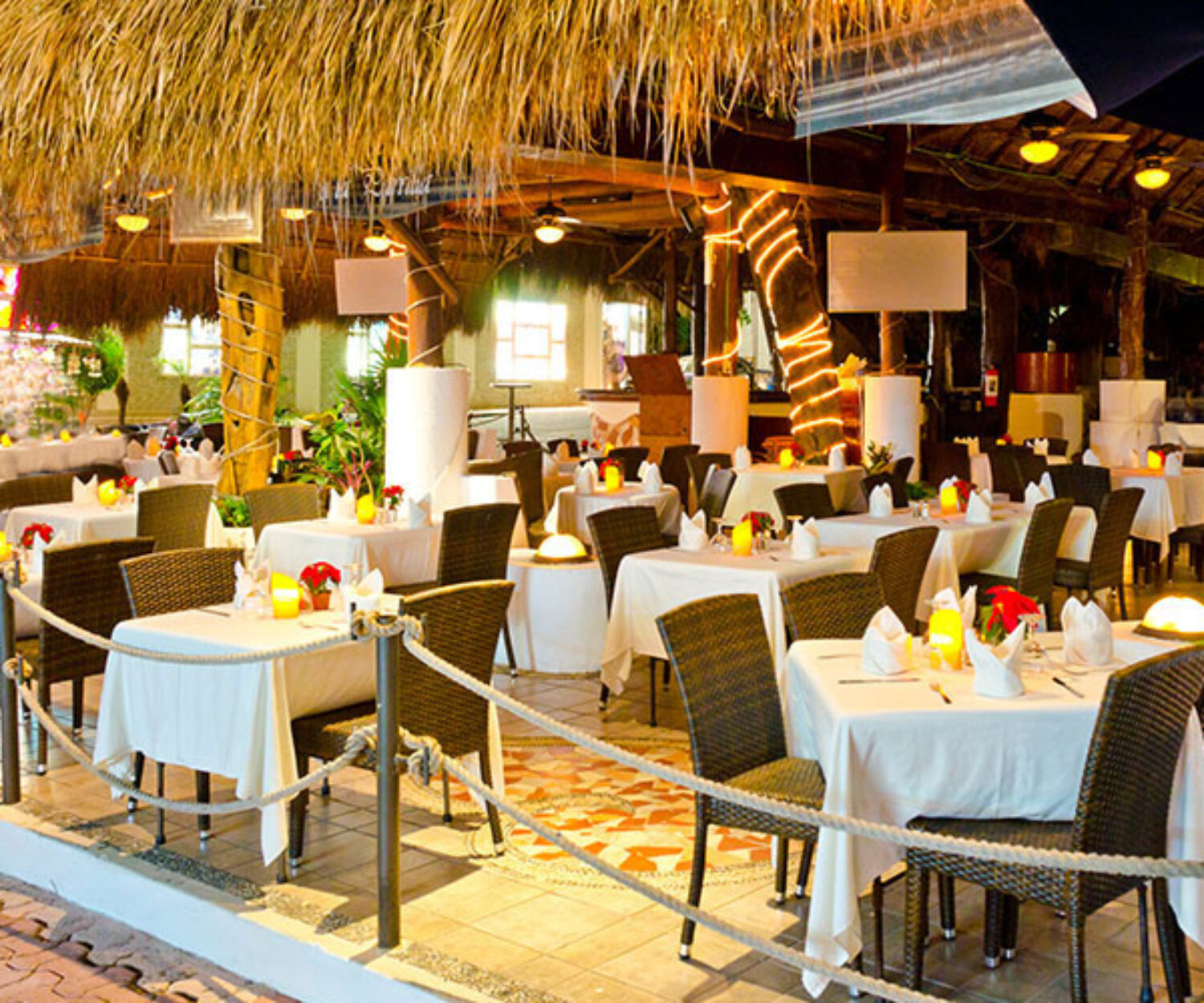 Elegant outdoor restaurant with neatly set tables under a thatched roof.