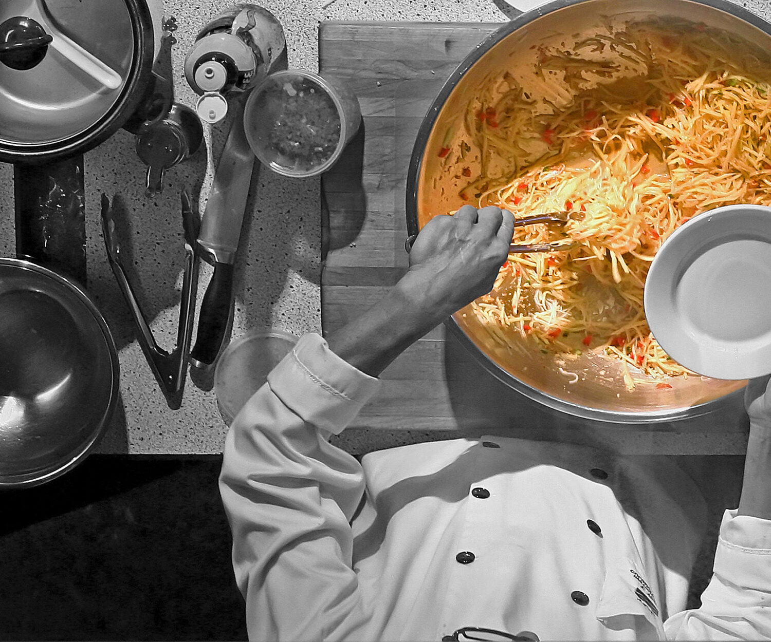 Chef seasoning a large pot of soup in a kitchen.