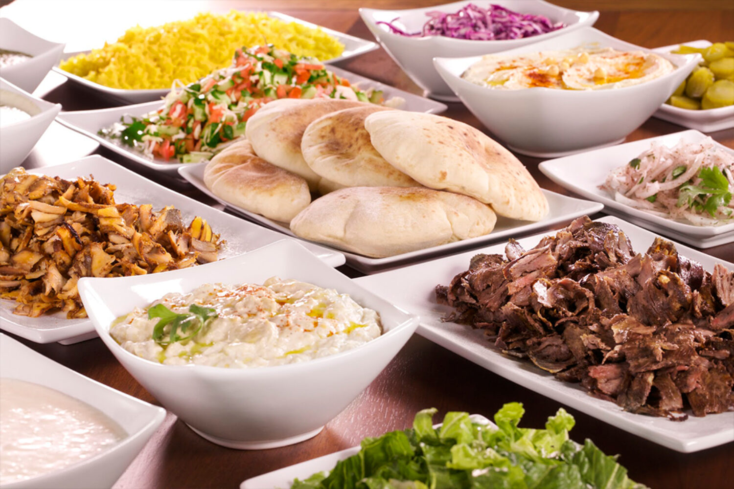 A Mediterranean feast with pita bread, salads, and grilled meat.