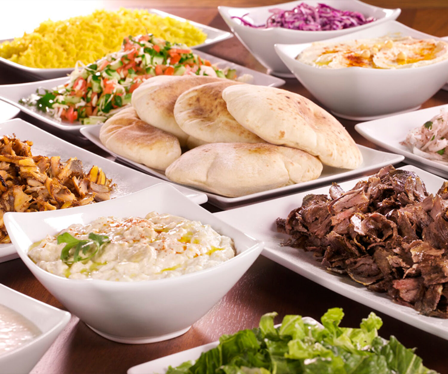 A Mediterranean feast with pita bread, salads, and grilled meat.