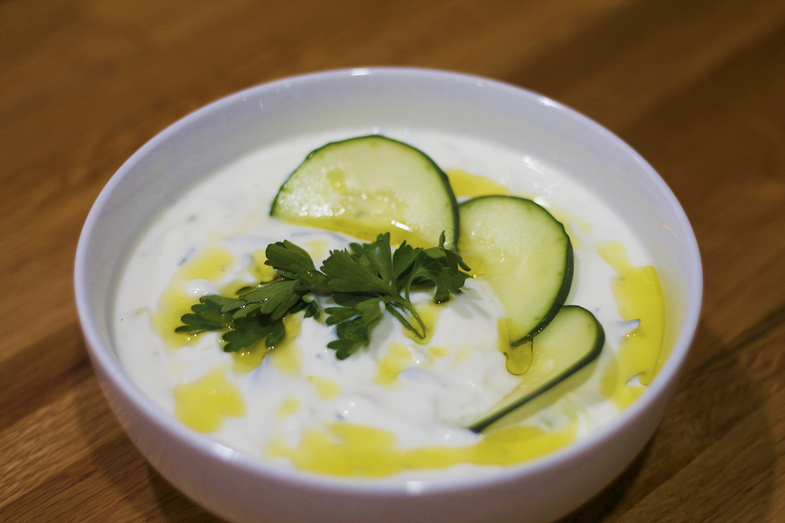 A bowl of tzatziki garnished with cucumber slices and parsley.